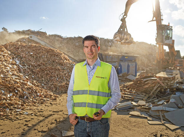 Mann mit gelber Warnweste und Funkgerät steht im Recyclingplatz in Brilon, Industriefotografie Christian Vorhofer 