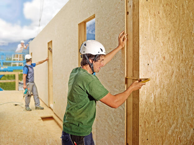 Zimmermann auf Baustelle misst mißt mit Zollstock und richtet OSB Wand ein, Industriefotografie Christian Vorhofer 